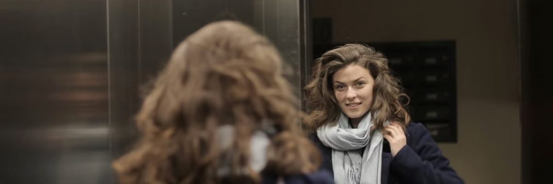 Stylish woman in an elevator admiring her reflection in the mirror while wearing a scarf.